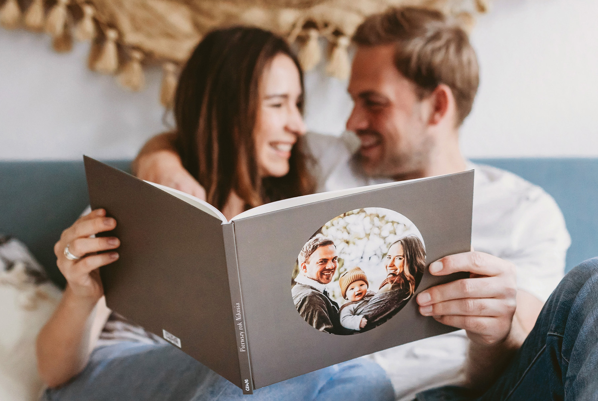 Para trzymająca otwarty, elegancko zaprojektowany fotoksiążkę z rodzinnych zdjęć, siedząc razem na kanapie. Para trzymająca otwarty, elegancko zaprojektowany fotoksiążkę z rodzinnych zdjęć, siedząc razem na kanapie.