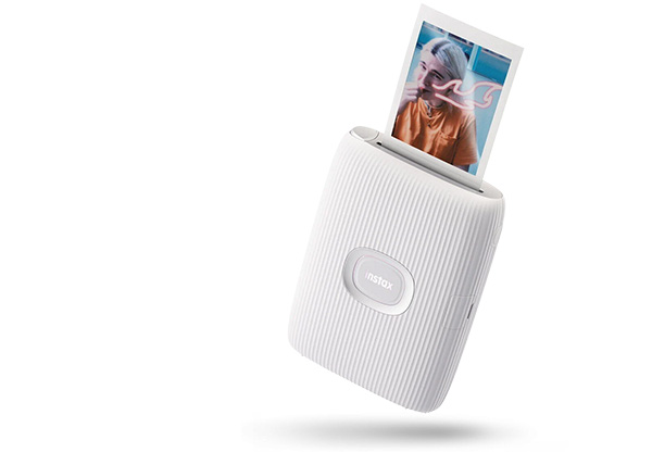 Biały, przenośny printer Instax z wysuwającym się zdjęciem w jasnych kolorach.