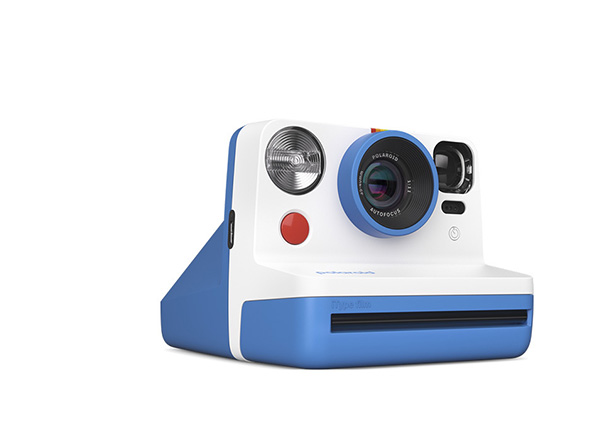 Biały aparat Polaroid z niebieską podstawą i kolorowym akcentem nad obiektywem, widok pod kątem