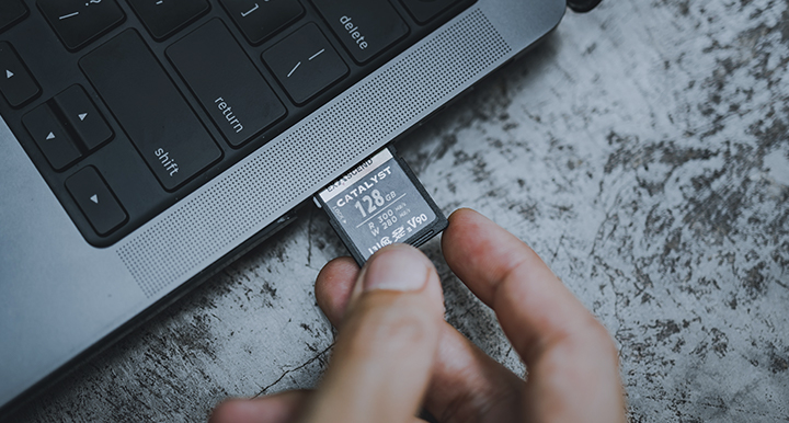 Dłoń wkładająca kartę pamięci SD o pojemności 128 GB do laptopa na stole z szarą, teksturowaną powierzchnią Dłoń wkładająca kartę pamięci SD o pojemności 128 GB do laptopa na stole z szarą, teksturowaną powierzchnią